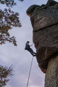 Side view of sportive male alpinist ascending on cliff in mountain terrain in cloudy day