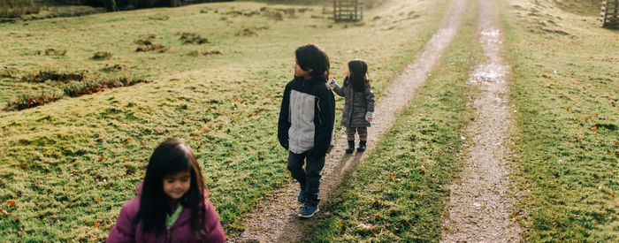 Siblings walking together on footpath amidst field