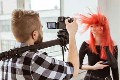 Rear view of man photographing young woman by window