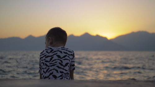 Boy sitting at beach during sunset