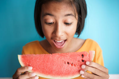 Close-up of teenage girl eating melon against wall