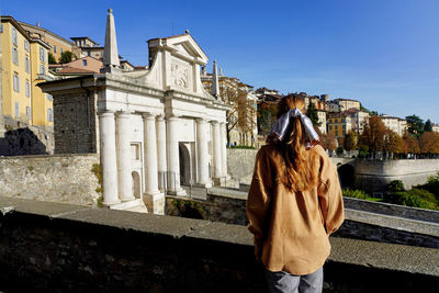 Back view of tourist girl in bergamo looking at porta san giacomo gate and venetian works of defence