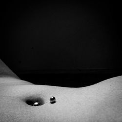 Midsection of woman with pierced stomach against black background