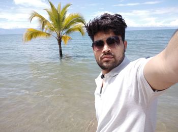 Portrait of young man standing at beach against sky