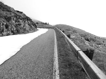 Empty road leading towards mountain against clear sky