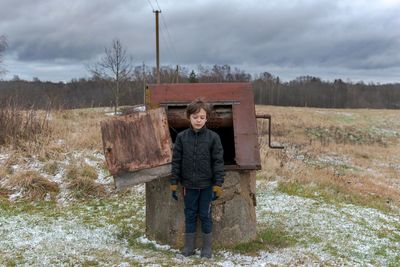 Portrait of kid, standing near well in snow covered land