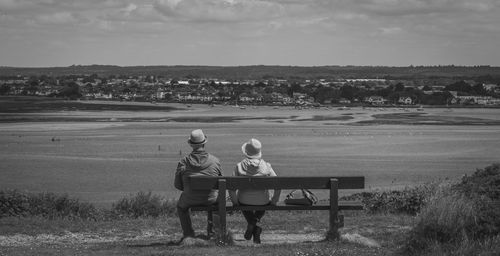 Rear view of couple sitting on bench against sky