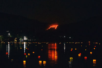 Illuminated city by river against sky at night