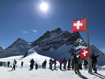 People and swiss flags on snowcapped mountain against clear blue sky