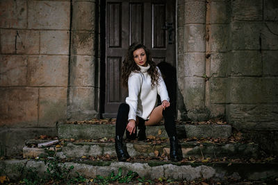 Full length portrait of woman sitting against building