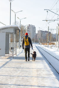 Rear view of man with dog walking in snow