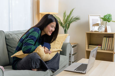 Young woman using laptop while sitting on sofa at home
