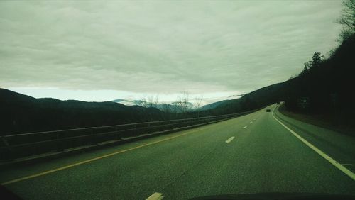 Empty road by mountains against cloudy sky