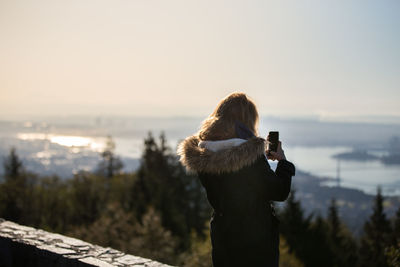 Man photographing with smart phone against sky during sunset