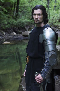 Portrait of knight standing by river in forest