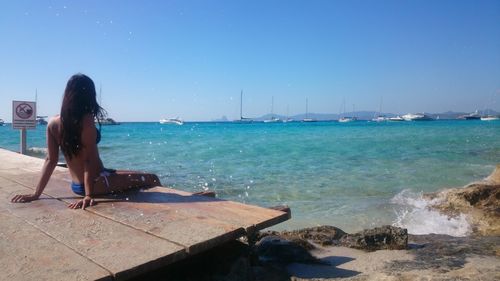 Woman sitting on shore by sea against sky