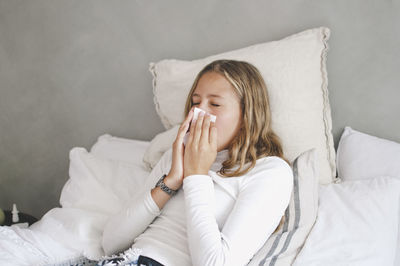 Girl blowing nose while lying on bed at home