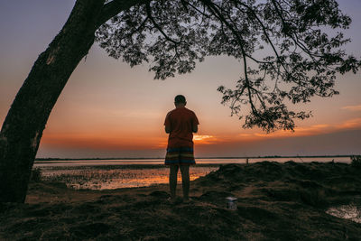 Rear view of man looking at sea during sunset