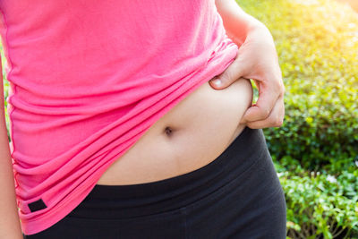 Midsection of woman pinching her belly outdoors