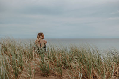 Woman standing on grass by sea against sky
