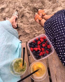 Low section of women sitting by fruits in container at beach