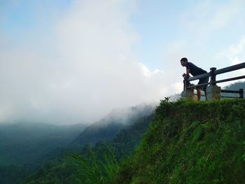 Man leaning on railing while standing at mountain peak against sky