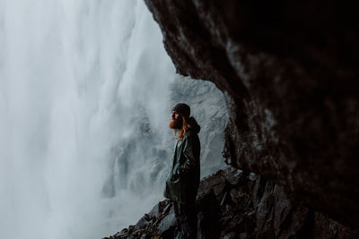 Side view of man standing on cliff against waterfall