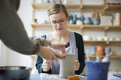 Female teacher assisting young woman in making pot in art class