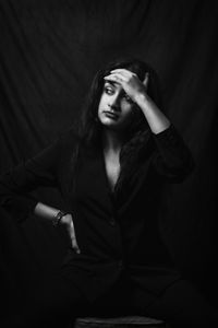 Portrait of young woman standing against black background