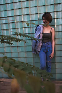 Young woman looking away standing against wall