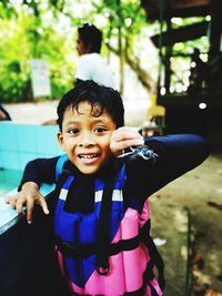 Portrait of cheerful boy wearing life jacket while standing at poolside