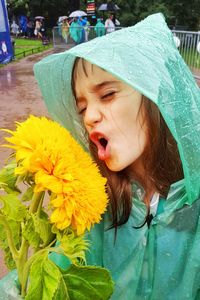 Girl in raincoat with yellow flower during rainy season on footpath at park