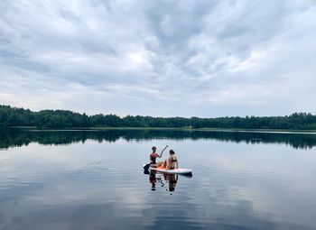 Two girls relaxing on sup paddle board on calm lake in summer