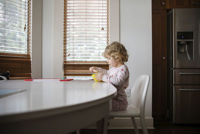 Side view of girl having food while sitting on chair at home