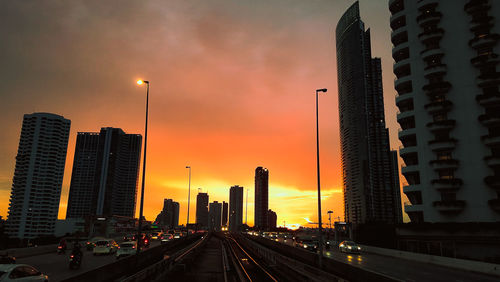 Road by buildings against sky during sunset in city