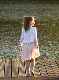 Rear view of girl standing on pier at lake