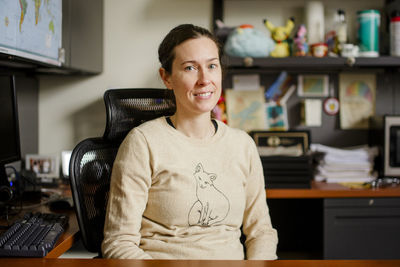 A woman professor sits in her office at a desk smiling