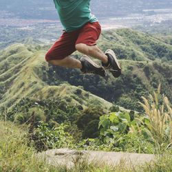 Low section of man jumping on mountain against sky