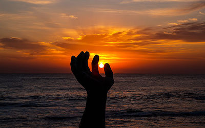 Silhouette hand holding sun during sunset