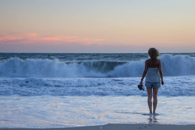 Rear view of woman standing at beach during sunset