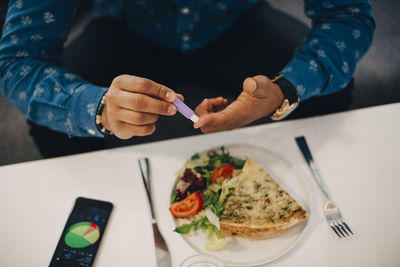 Midsection of businessman checking blood sugar level while having food at table