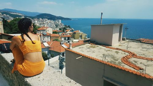 Rear view of woman looking at sea by buildings against sky