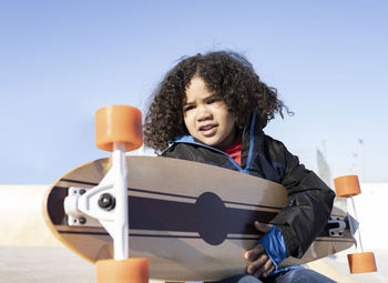 Boy holding toy sitting against clear sky