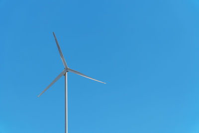 Low angle view of wind turbine against blue sky