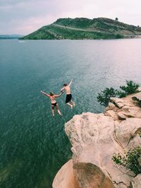 Rear view of couple jumping from cliff in sea