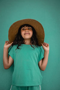 Portrait of girl in green t-shirt and straw hat against green wall