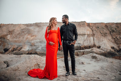 Rear view of couple standing on red rock against sky