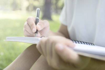 Close-up of woman writing on book in park