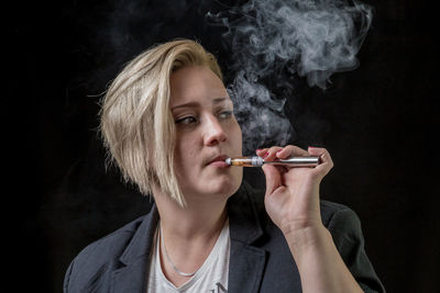 Close-up portrait of a young woman smoking over black background