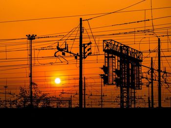 Silhouette electricity pylon against orange sky